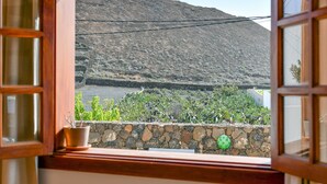 Una finestra con vista su un paesaggio montuoso, un muro in pietra e una pianta in vaso.
