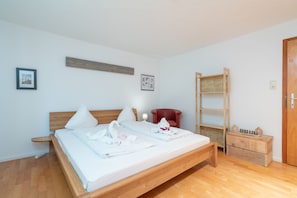A clean, modern bedroom with a wooden bed, a red chair, a wooden ladder, and a small wooden dresser.
