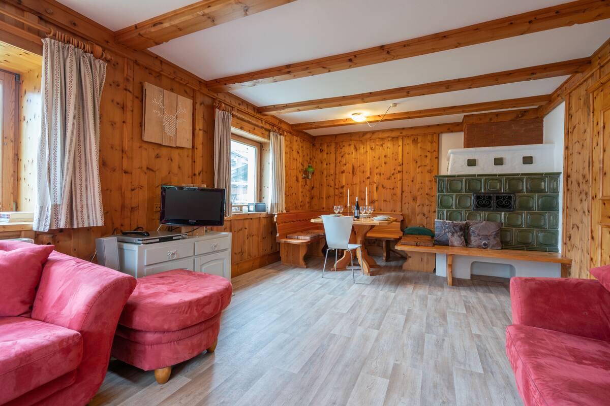 A cozy room with wooden walls and floors, a television, a dining table with chairs, and two pink sofas.