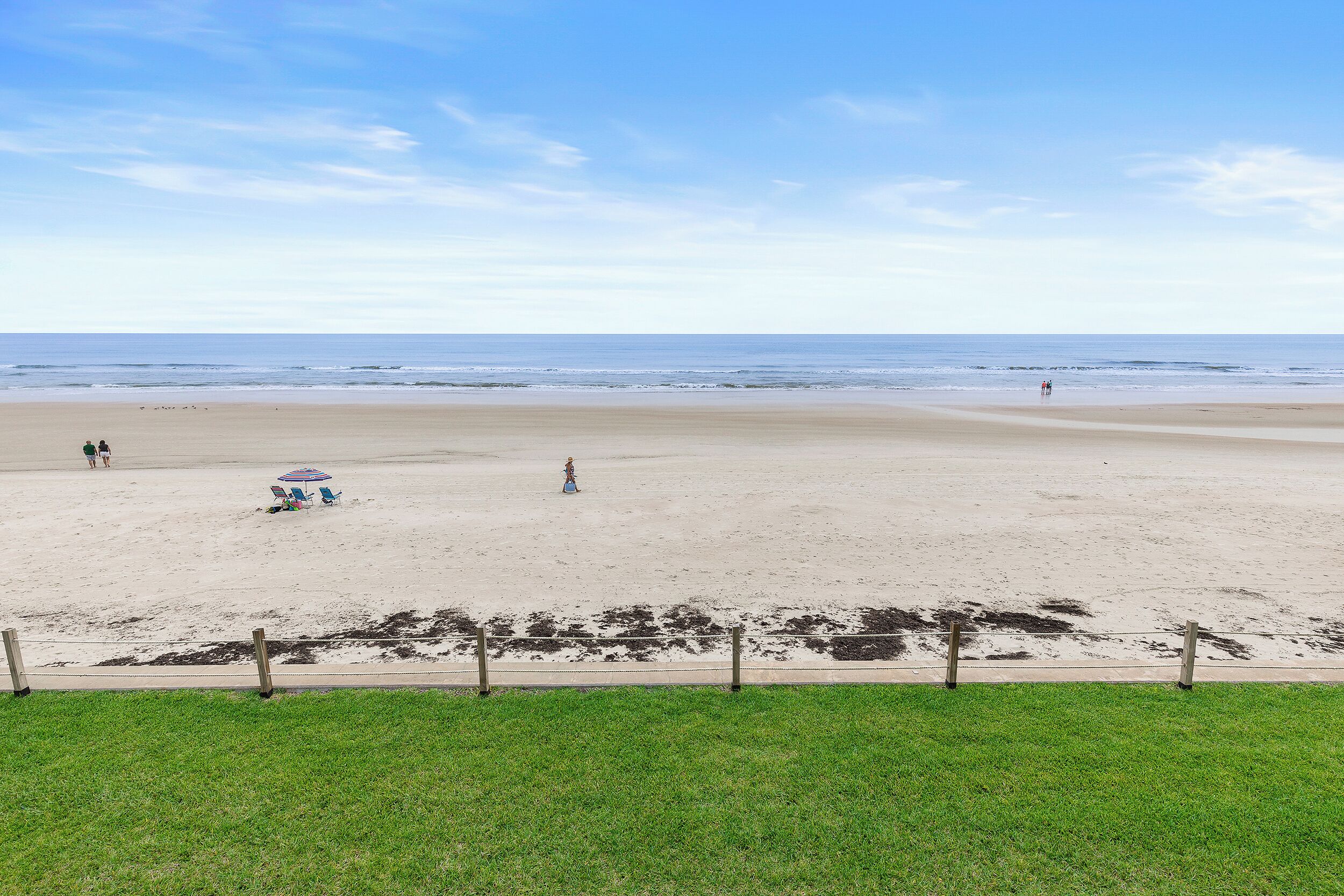 A beach with a grassy foreground, a sandy beach, and a clear sky.