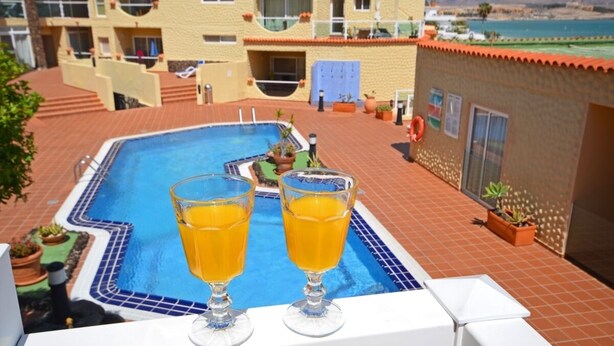 A pool area with two glasses of orange juice on a terrace. - Apartment PLAYA 2 -sea view -2 bedrooms -WiFi -pool (Costa Calma)