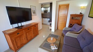 A living room with a TV, wooden cabinet, wicker ottoman, and purple sofa. - Apartment PLAYA 2 -sea view -2 bedrooms -WiFi -pool (Costa Calma)