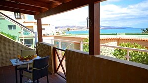A balcony with a table set for breakfast, overlooking a coastal view with buildings and a beach. - Apartment PLAYA 2 -sea view -2 bedrooms -WiFi -pool (Costa Calma)