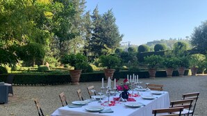 An outdoor dining area with a table set for six, surrounded by chairs, in a garden setting with potted plants and trees. - Elegant 3 bedroom apt, in historical Villa, shared pool, parking, 3km to Center (Florence)
