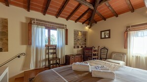 A bedroom with a large bed, wooden headboard, a stone wall, a wooden desk, and a chair. - Elegant 3 bedroom apt, in historical Villa, shared pool, parking, 3km to Center (Florence)