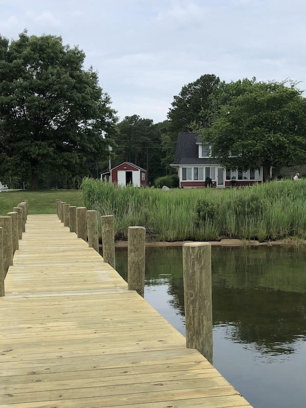 A wooden dock leading to a house by a calm body of water, surrounded by lush greenery.