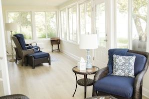 A room with wicker furniture, a lamp, and a view through large windows.