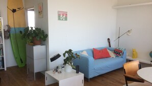 Een woonkamer met een blauwe bank, een surfplank, een lamp en een kat.