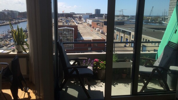 Een balkon met uitzicht op een jachthaven en gebouwen, een bloempot en een stoel.