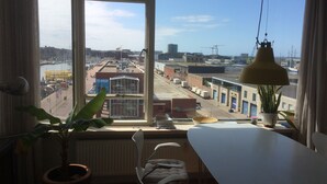 Een kamer met een groot raam met uitzicht op een stadsbeeld, een witte tafel, een stoel en een hanglamp.