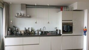 Een moderne keuken met witte kasten, een zwart aanrecht en roestvrijstalen apparatuur. Er zijn hanglampen, een inbouwoven en een raam met gordijnen.