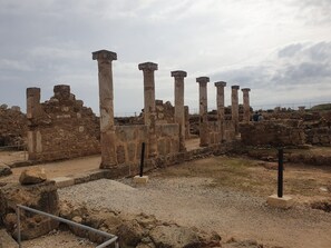 Ancient ruins with stone columns and walls, a gravel path, and a fenced area.