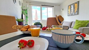 Une table dressée pour le petit-déjeuner, avec des croissants, des fraises et du jus d’orange, et une vue sur l’extérieur.
