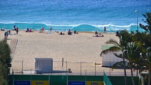 Une plage où l’on peut voir des gens bronzer et se baigner, une tour de surveillance pour les sauveteurs et une clôture ornée de panneaux publicitaires.