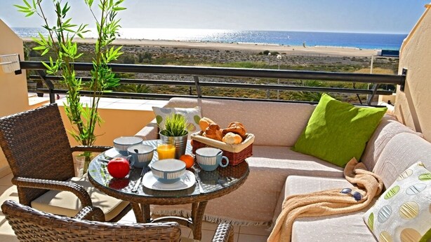 Un balcon agrémenté de meubles en osier, une table mise pour le petit-déjeuner et une vue sur la plage.