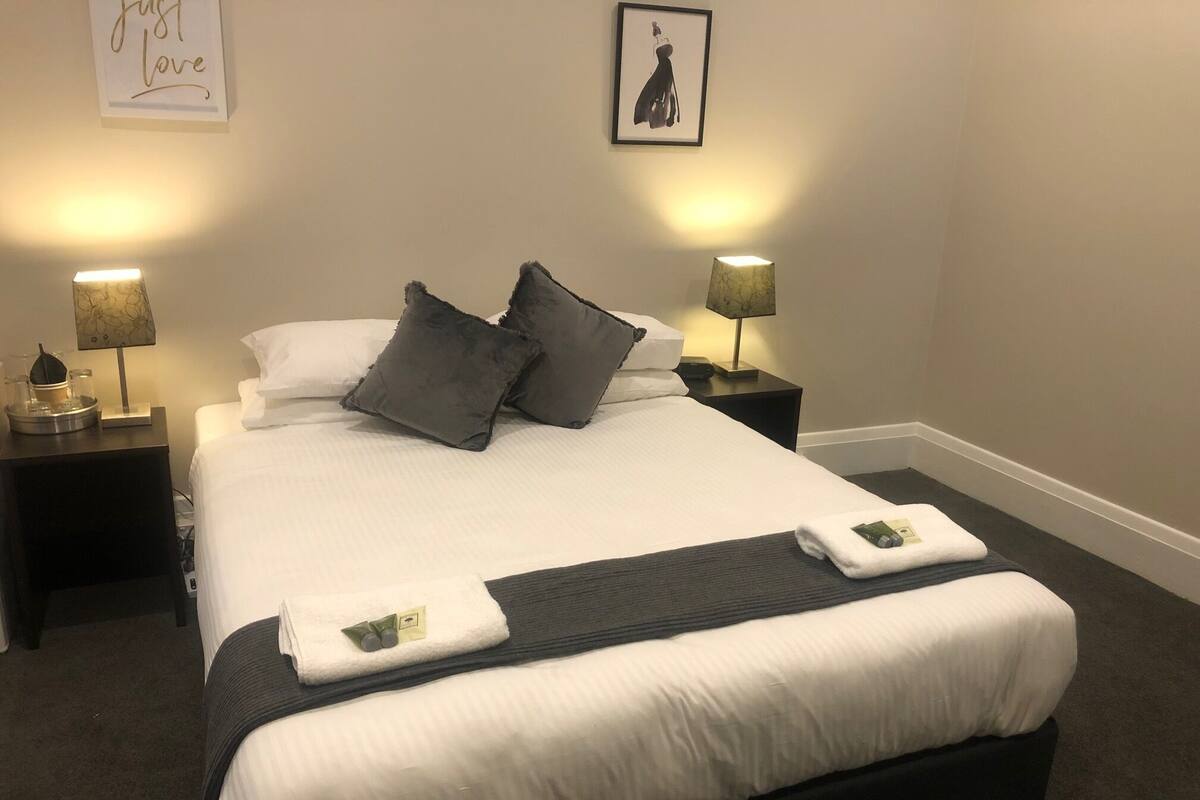 A neatly made bed with pillows, two bedside lamps, and a framed picture on the wall.