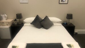 A hotel room with a bed, two bedside tables, a clock, and a sign on the wall. - Wentworth Hotel (Homebush)