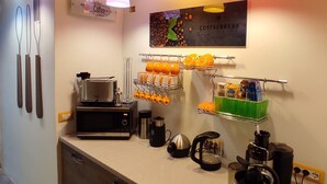 Uma cozinha compacta com cafeteira, chaleira e canecas laranja em um suporte.