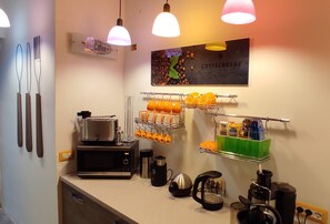 Une petite cuisine équipée d’une machine à café, d’une bouilloire et de tasses oranges rangées sur un présentoir.