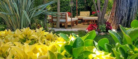 A garden with a wooden table and chairs, surrounded by various plants and flowers.