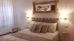 Quarto com cama, duas mesas de cabeceira, uma obra de arte na parede e uma janela com cortinas leves.