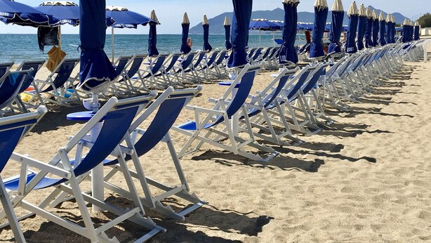 Uma praia com fileiras de cadeiras de praia azuis e brancas e guarda-sóis combinando.