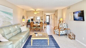 Een ruime woonkamer met een bank, salontafel en stoelen, een eethoek met een tafel en stoelen, en een keuken op de achtergrond.
