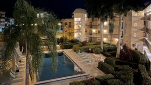 Een hotel met een zwembad, palmbomen en een goed verlichte gevel.