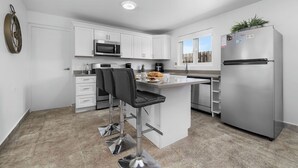 A modern kitchen with white cabinets, stainless steel appliances, and a central island with bar stools. - ModernPrivatePoolQuiet3BR2BA Eagle/Palm Beach (Noord)