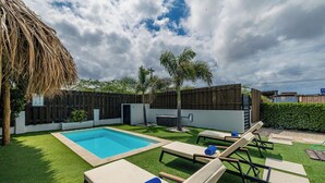 A backyard with a swimming pool, lounge chairs, and a wooden fence. - ModernPrivatePoolQuiet3BR2BA Eagle/Palm Beach (Noord)