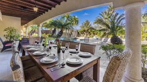 Un comedor al aire libre con una mesa de madera dispuesta para seis personas, rodeada de sillas de mimbre.