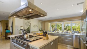 Una cocina moderna con una isla central, electrodomésticos de acero inoxidable y vistas al exterior a través de amplios ventanales.