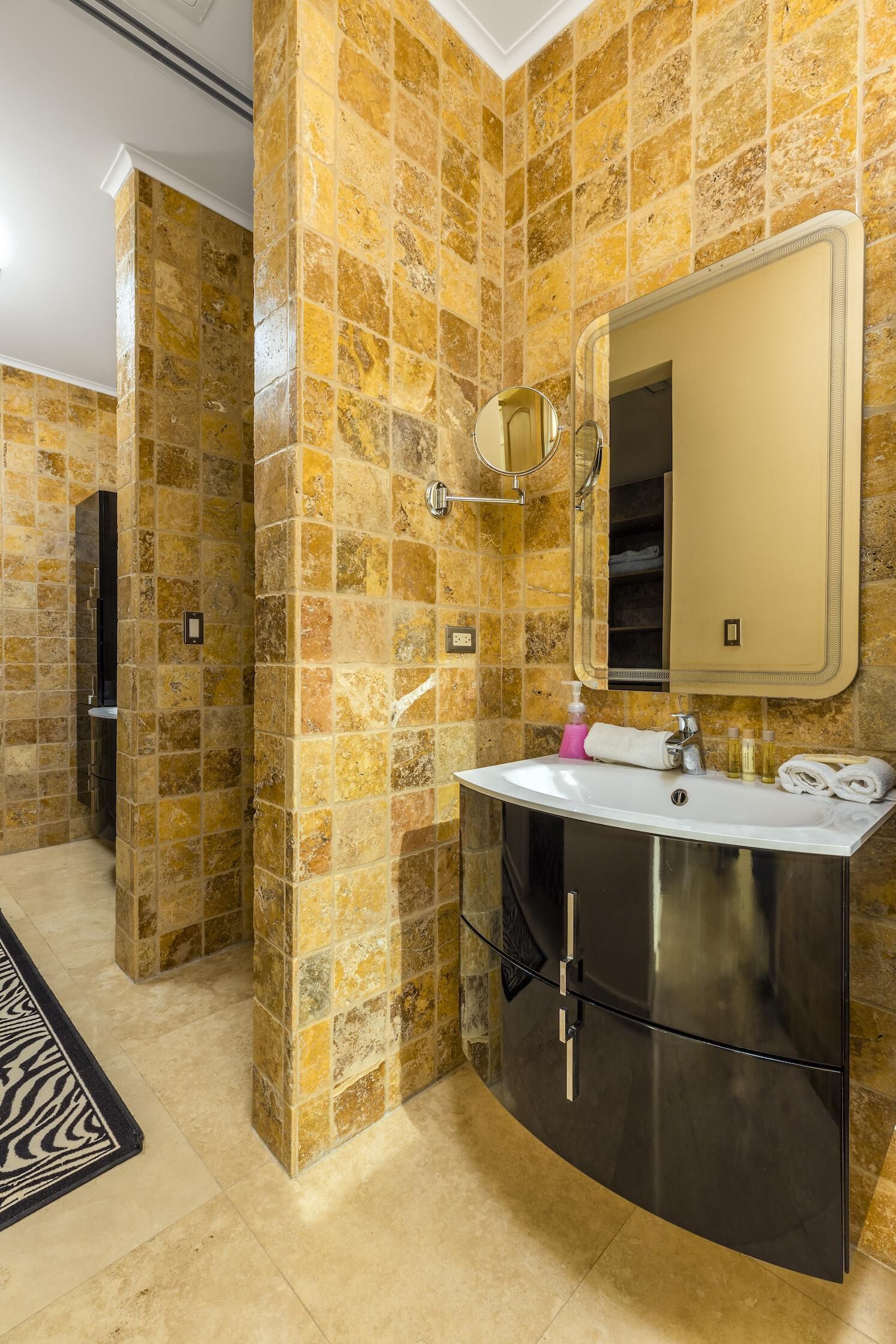 A bathroom with a stone wall, a sink with a mirror, and a black cabinet.
