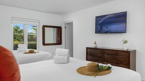 Une chambre d’hôtel avec deux lits, une grande télévision, une armoire en bois et une vue sur la verdure.