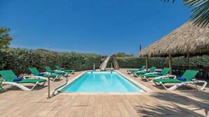 Un espace piscine avec des chaises longues et une structure dotée d’un toit de chaume.