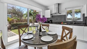 Une cuisine moderne avec des meubles blancs, une grande fenêtre et un coin repas comprenant une table ronde et des chaises.