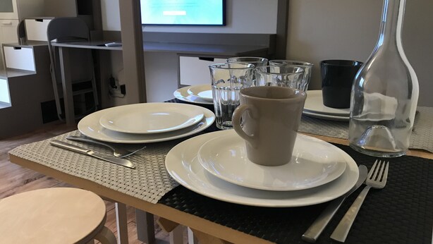 Une table à manger dressée avec des assiettes, une tasse, des couverts et une bouteille d’eau.