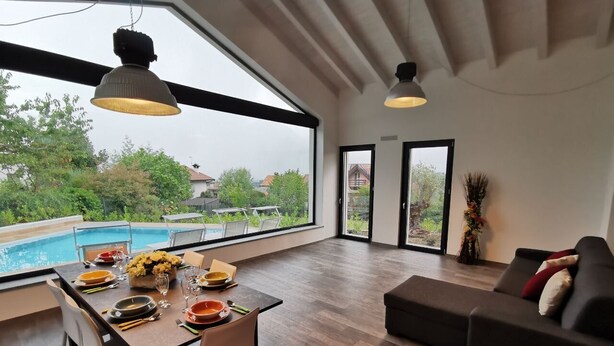 A spacious living room with a dining area, large windows, and a view of a swimming pool. - Villa Vittoria - POOL  (Colico Piano)
