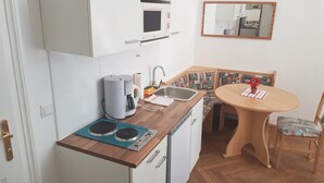 Angolo cottura compatto con microonde, bollitore e bollitore sul piano di lavoro. Presente un lavello, un piccolo tavolo con una sedia e uno specchio a parete.