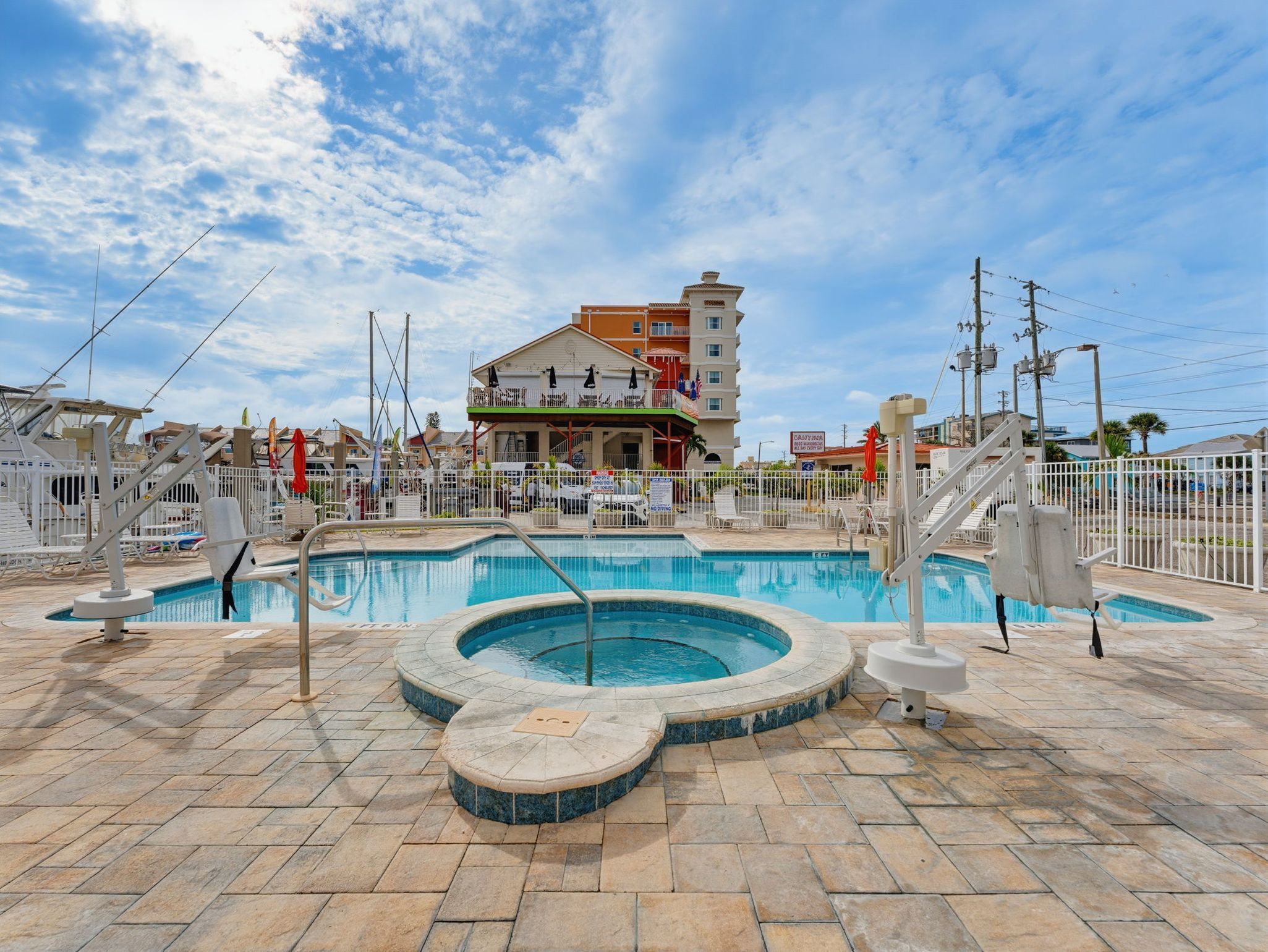 A swimming pool area with a hot tub, lounge chairs, and a building with balconies in the background.