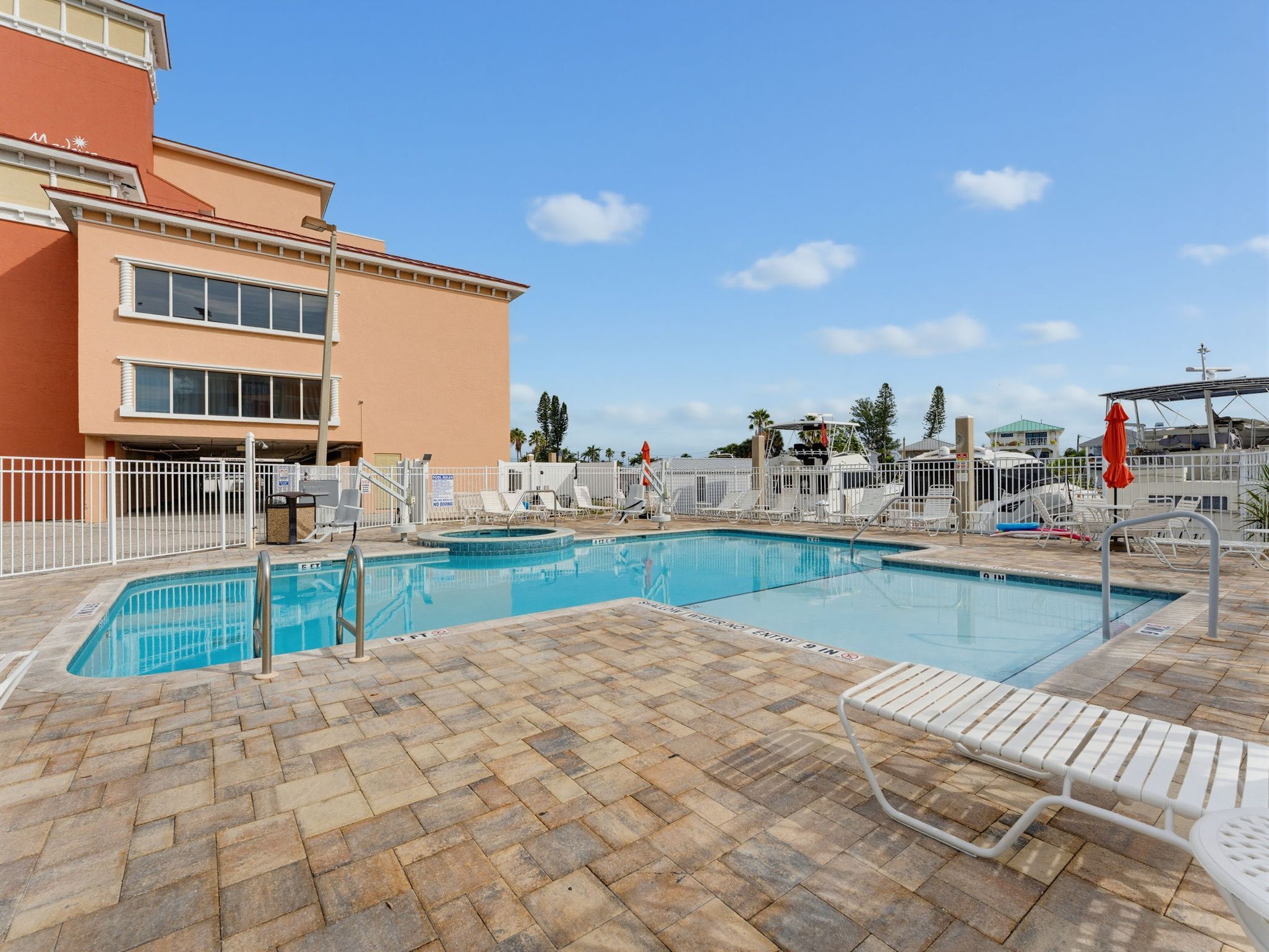 Un espace piscine comprenant deux piscines, des chaises longues et un bâtiment en arrière-plan.