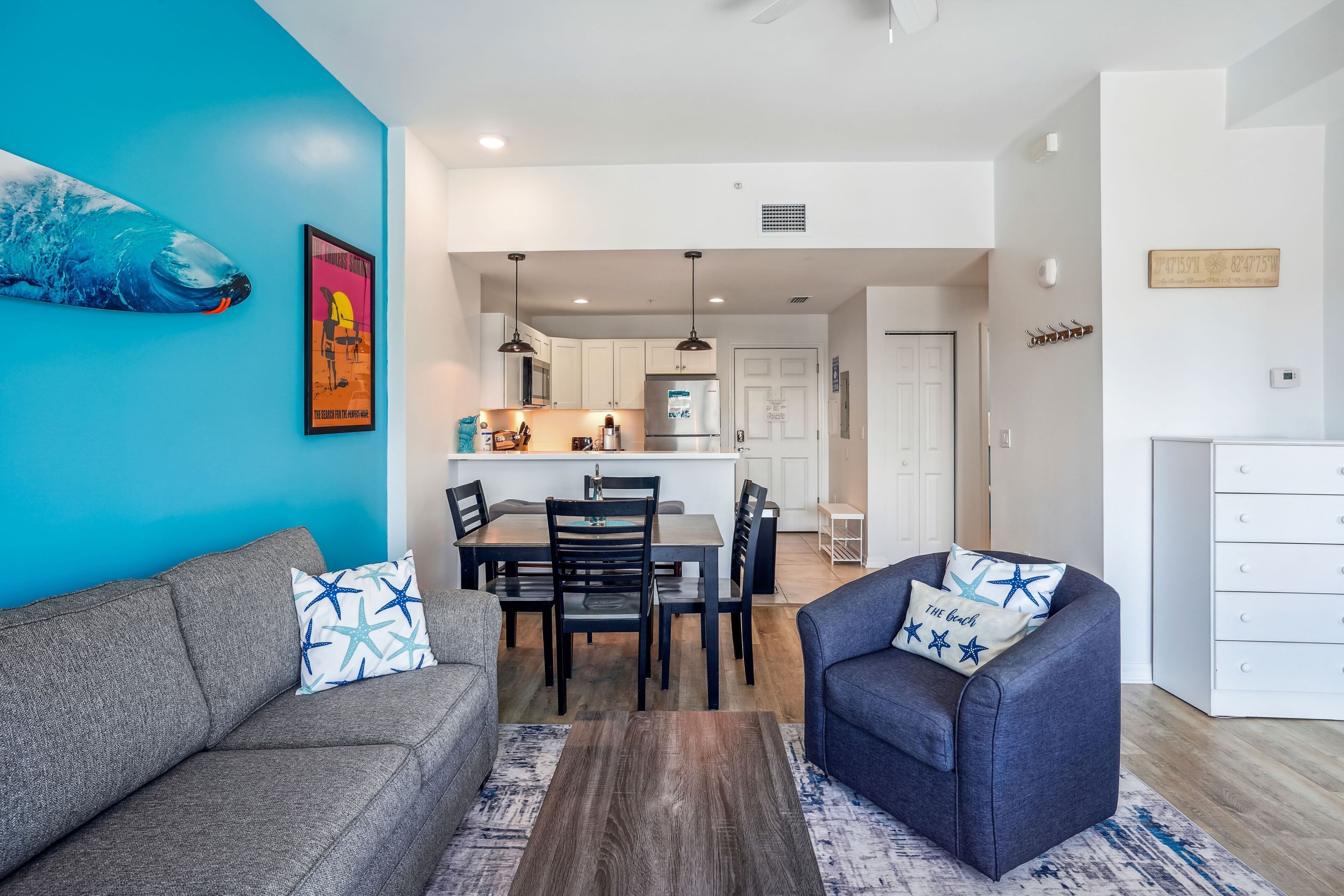 A modern living room with a grey sofa and armchair, a wooden coffee table, and a blue wall with a whale mural.