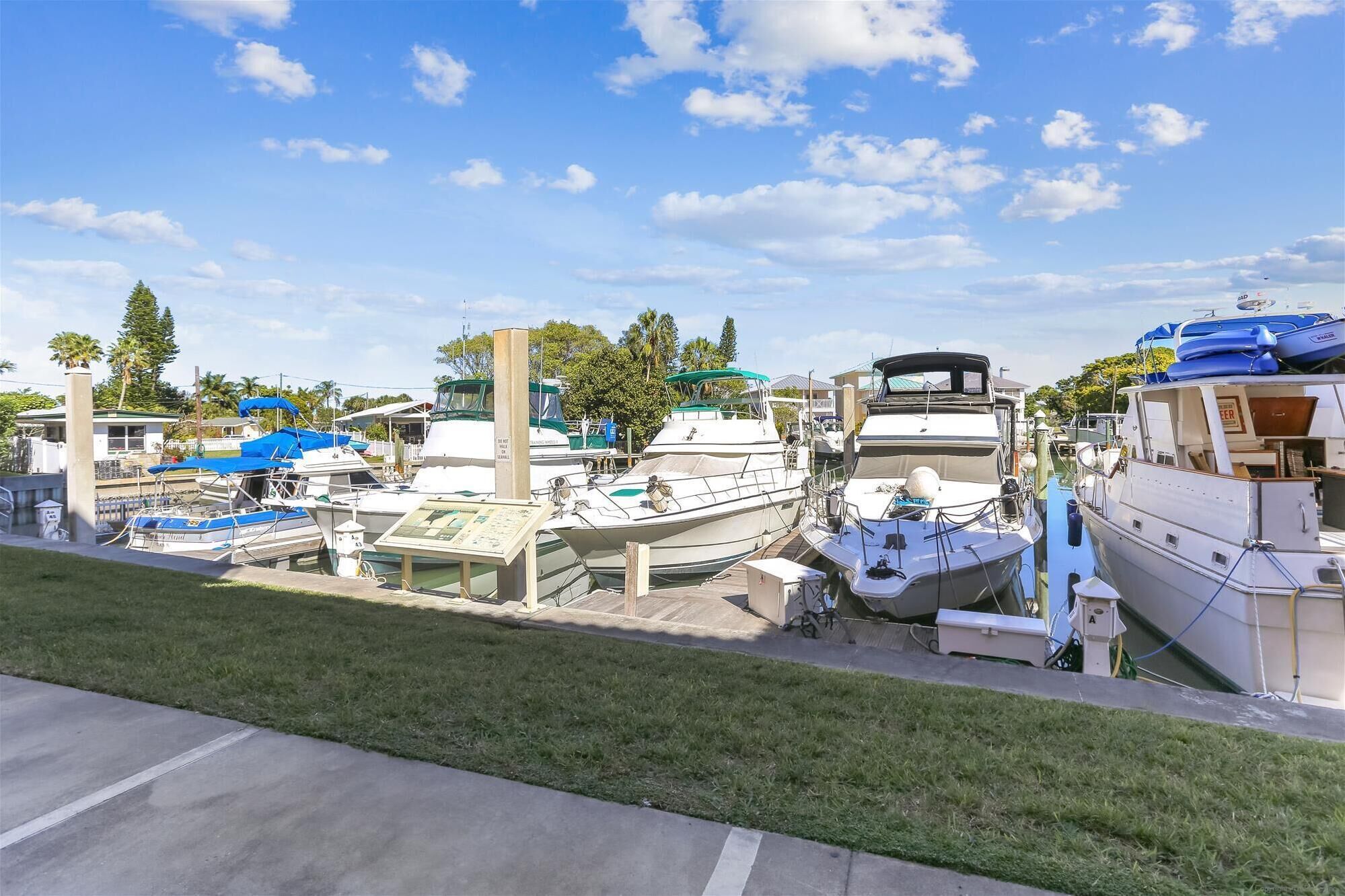 A marina with various boats docked, a grassy area in the foreground, and a clear sky.