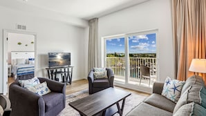 A modern living room with a large sliding glass door to a balcony, a flat-screen TV, and two sofas with star-patterned pillows.