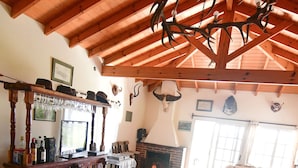A rustic interior with a wooden ceiling, a fireplace, a bar area, and a dining table set with a meal.
