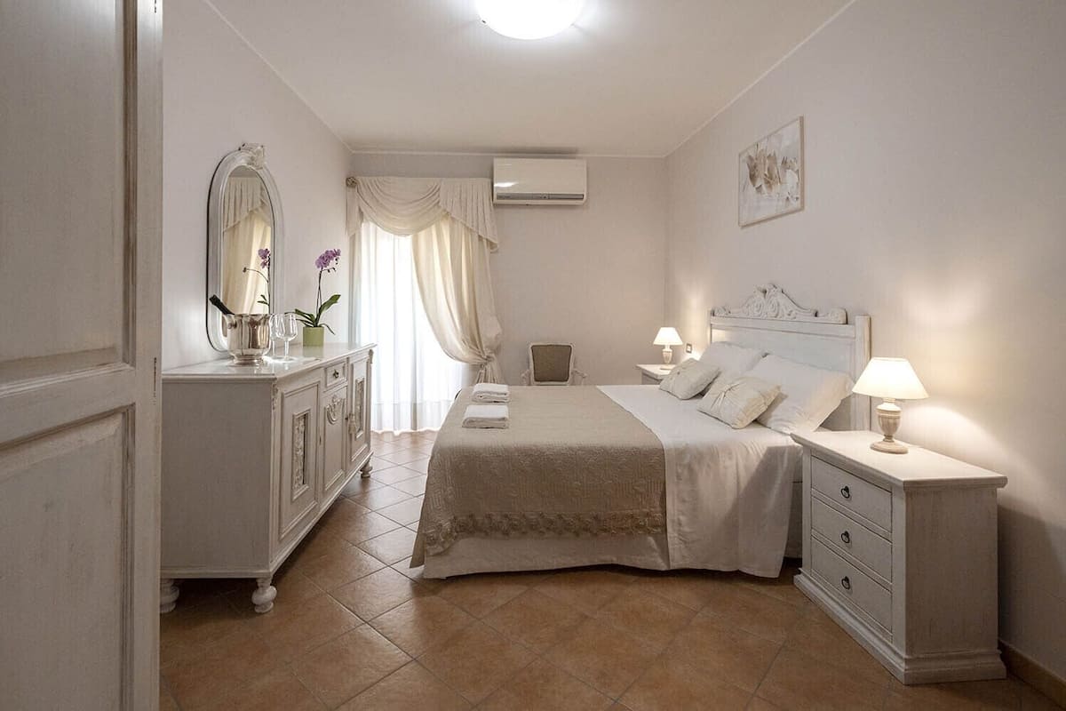 A bedroom with a bed, nightstands, a dresser, a mirror, and an air conditioning unit.