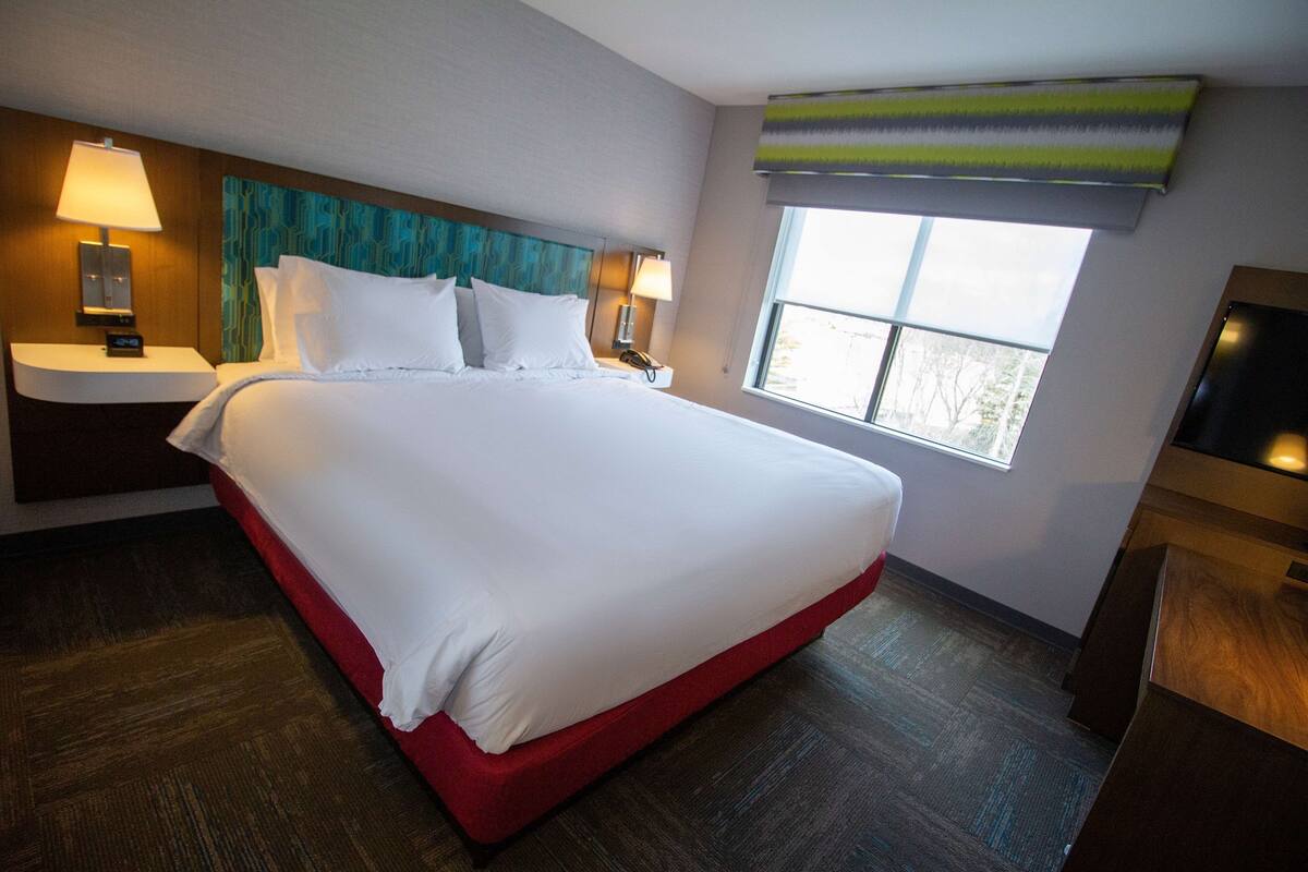 A hotel room with a large bed, two bedside tables with lamps, a TV, and a window with a view.