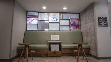 A waiting area with a green sofa, two wooden tables, a printer, and a window with colorful artwork.