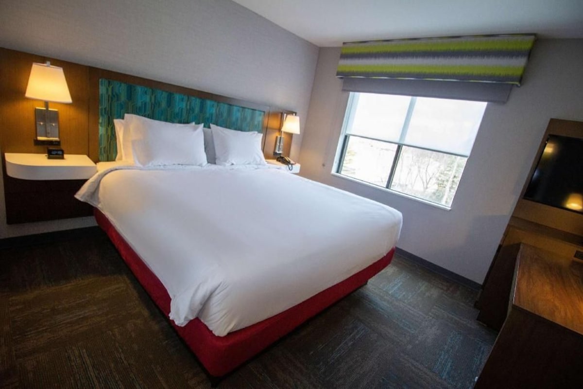 Una camera d'albergo con un letto grande, due comodini, una TV e una finestra con vista.
