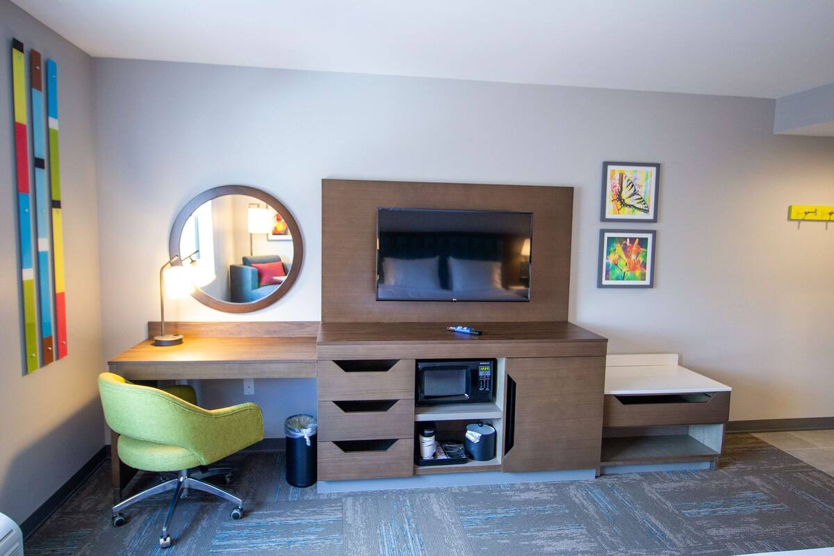 A modern hotel room with a desk, chair, TV, and artwork.